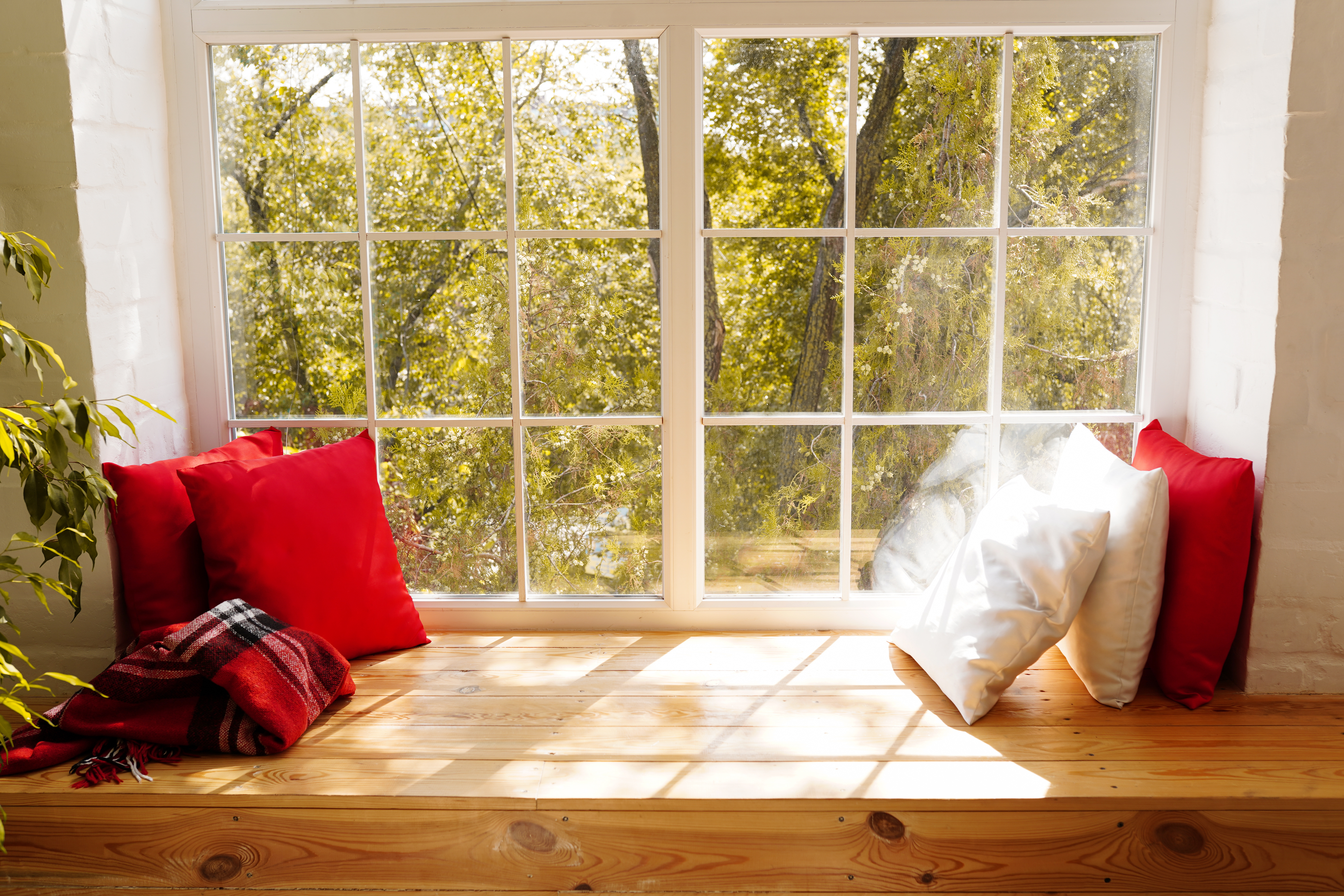 Fensterbank Massivholz breit als Sitzfensterbank mit roten und weißen Kissen vor Sprossenfenster, Blick in den Garten