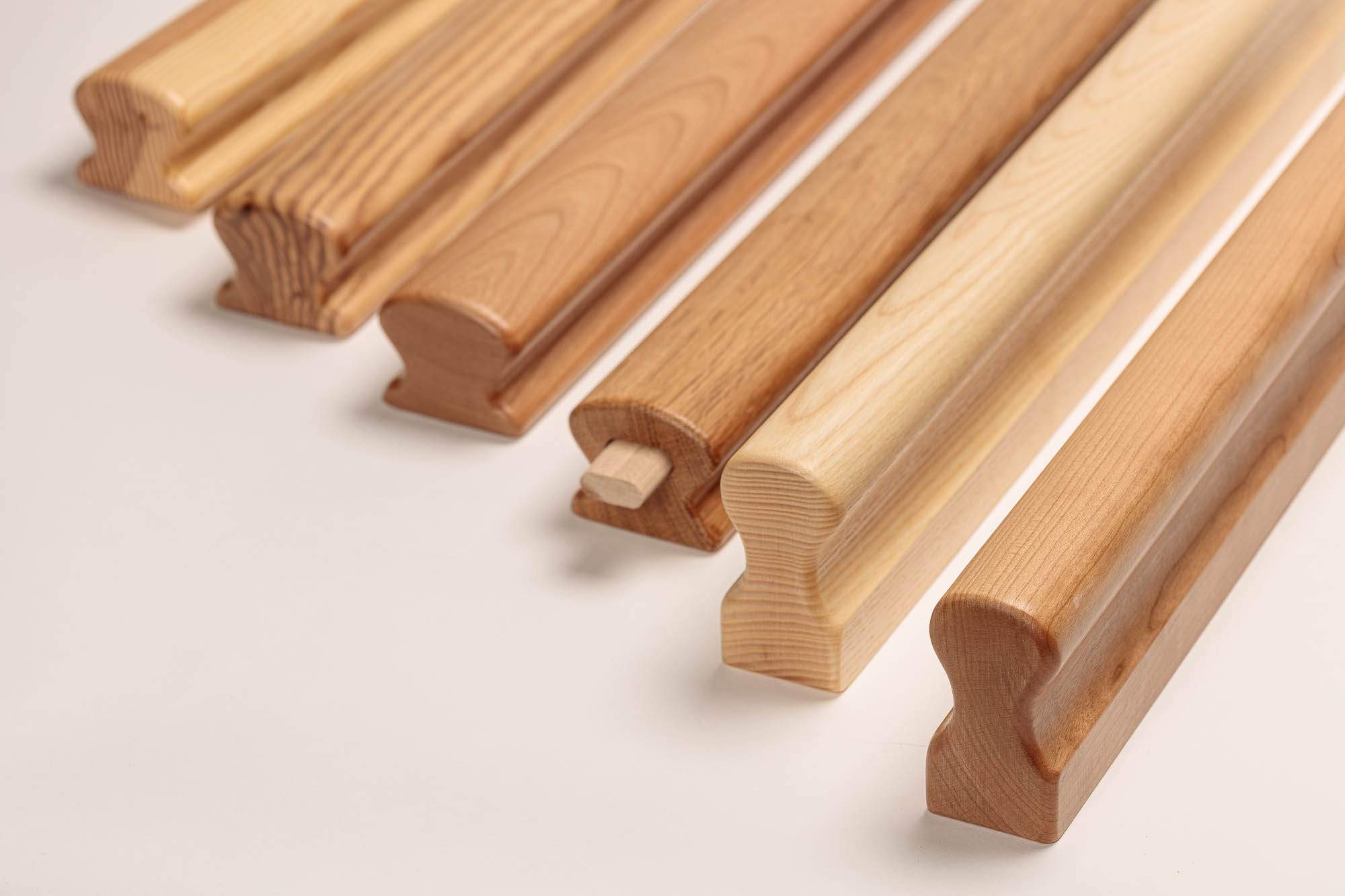 Holzhandläufe omega in sechs Holzarten nebeneinander, helle bis rötliche Hölzer, Omega-Profil mit Griffmulde sichtbar