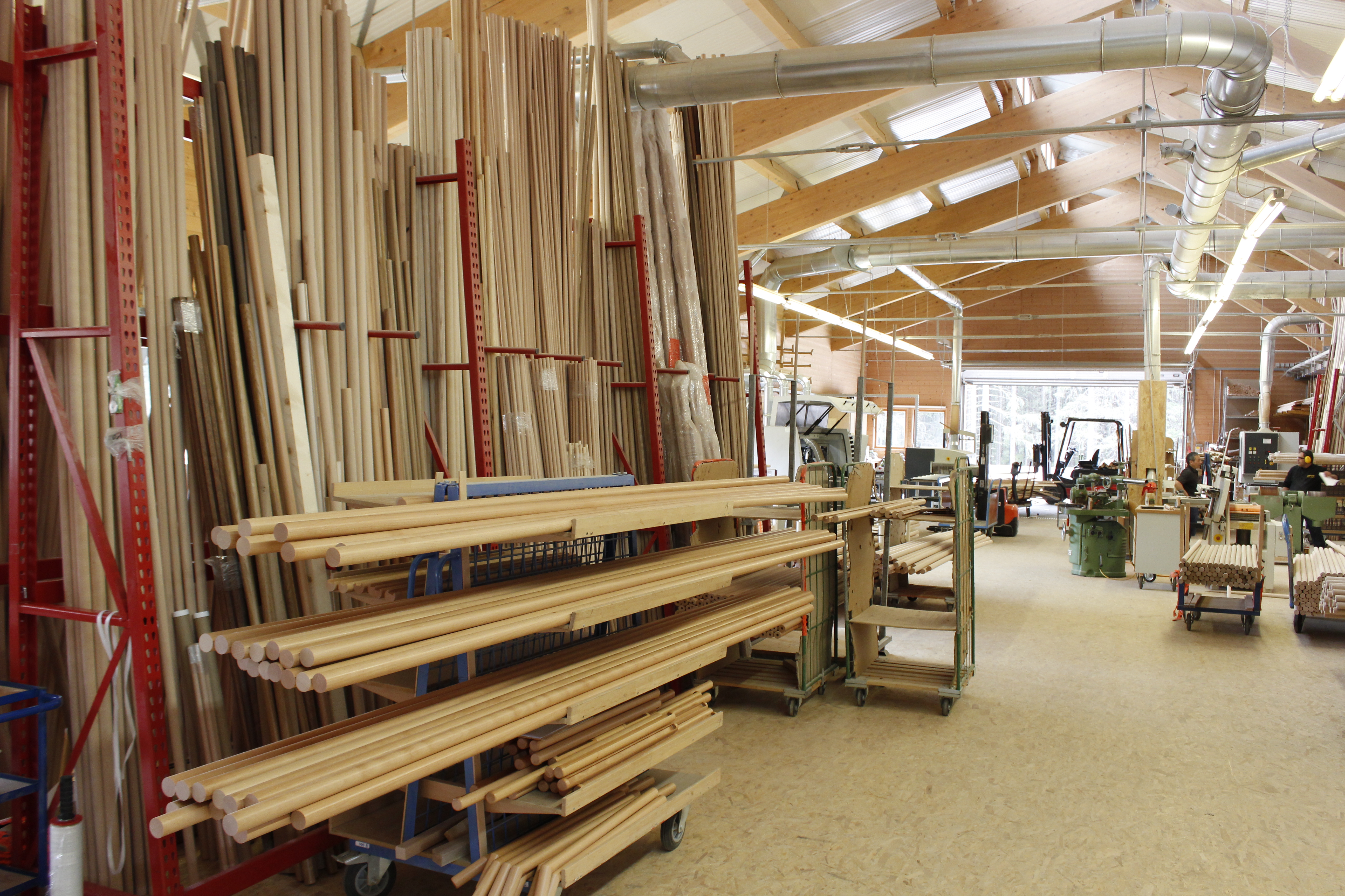Holzhandläufe und Rundstäbe im Lager der Drechslerei, lange Holzstäbe in roten Kragarmregalen in der Werkhalle