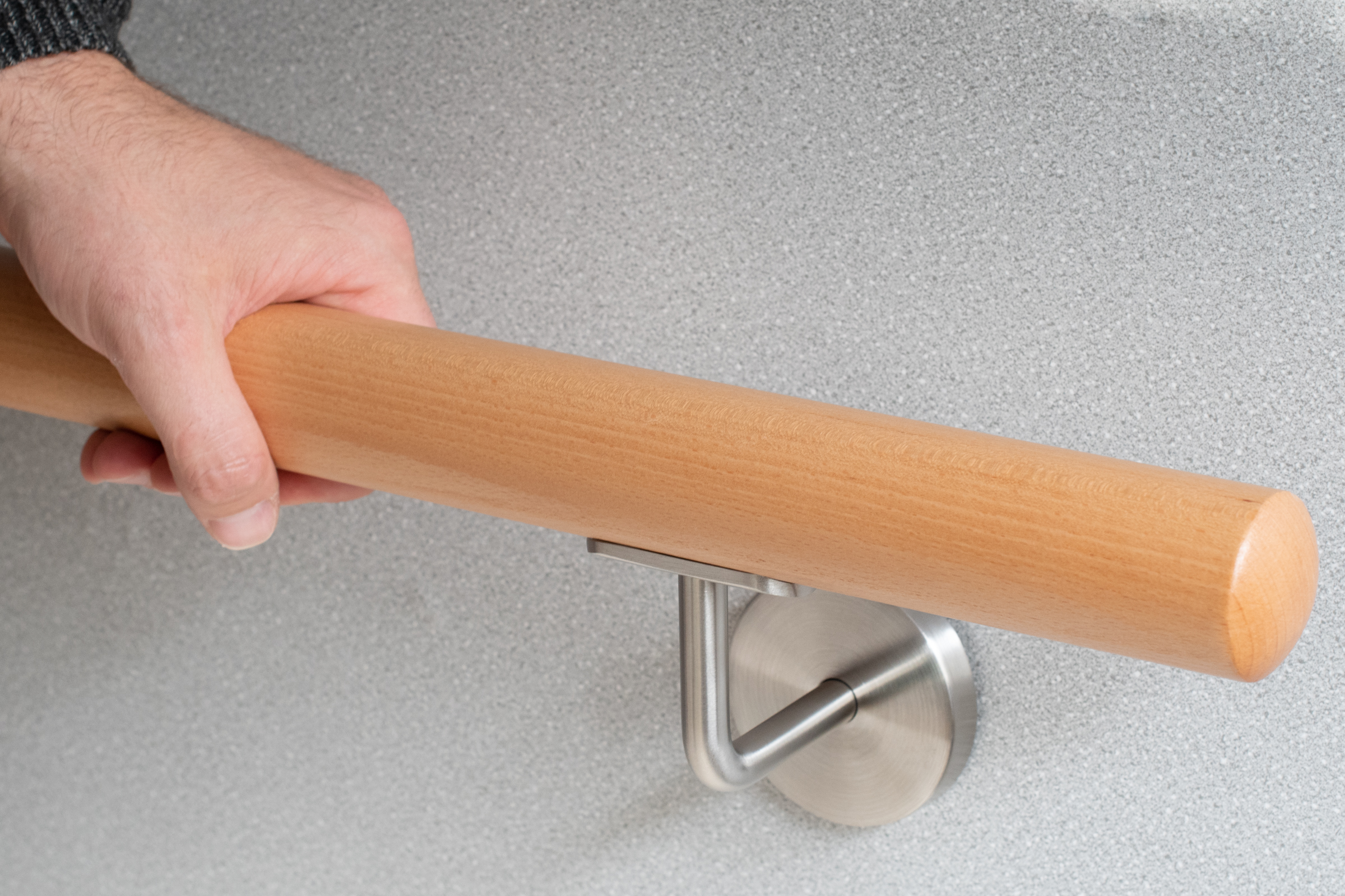 Handlauf rund Buche an grauer Wand mit Edelstahl-Handlaufhalter, Hand greift den Handlauf, Griffdetail