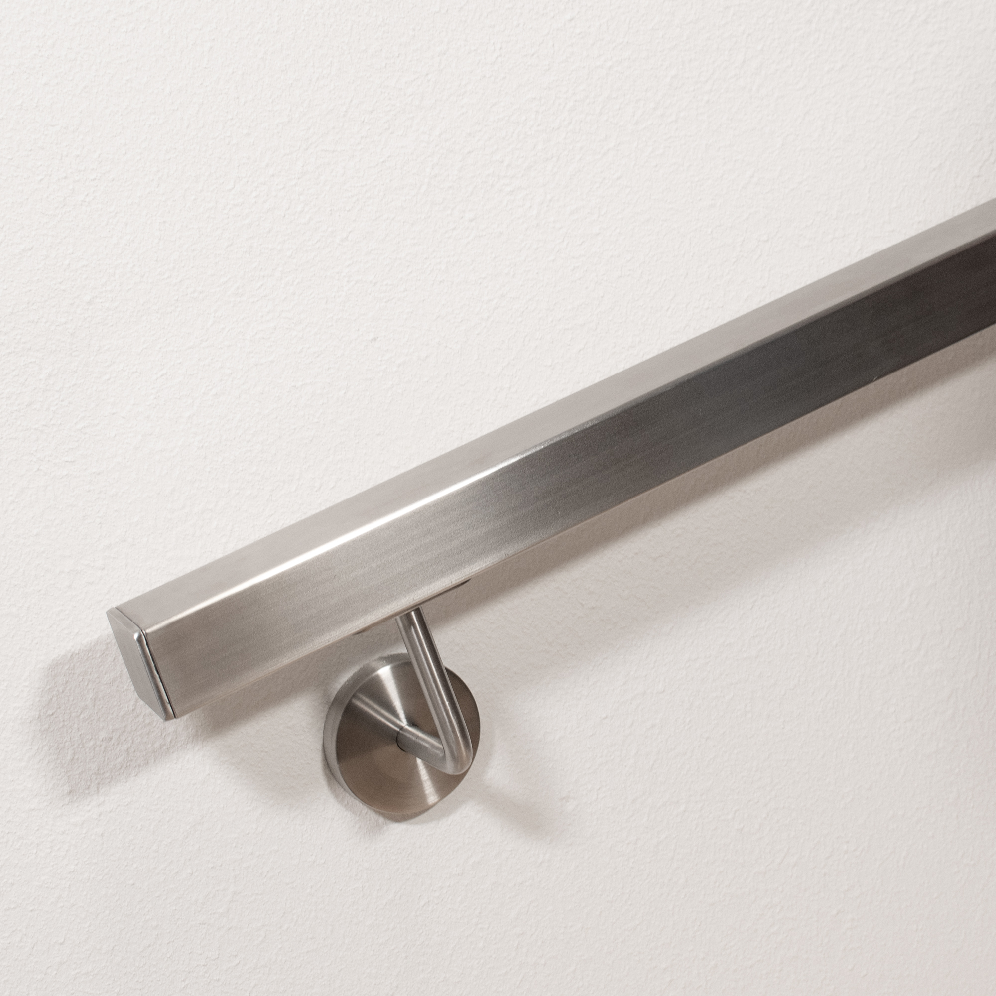Handlauf Edelstahl quadratisch mit flacher Endkappe und gebogenem Wandhalter, Handlaufende im Detail an weißer Wand