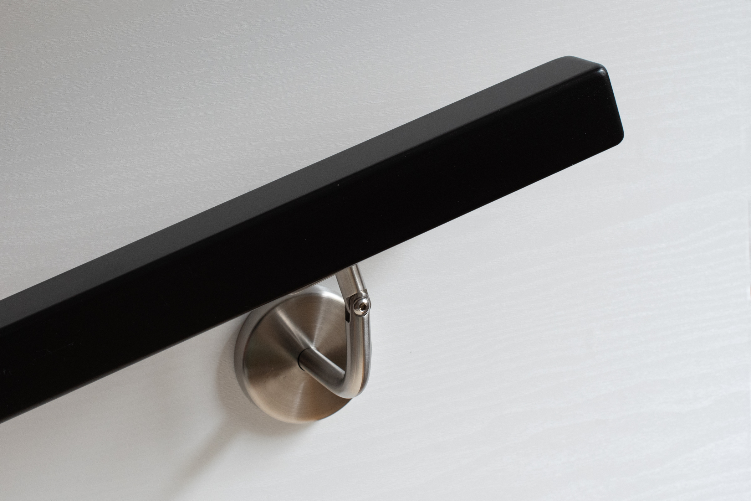 Handlauf quadratisch schwarz lackiert mit Edelstahl-Wandhalter an weißer Holzwand, matte Oberfläche, Schrägansicht