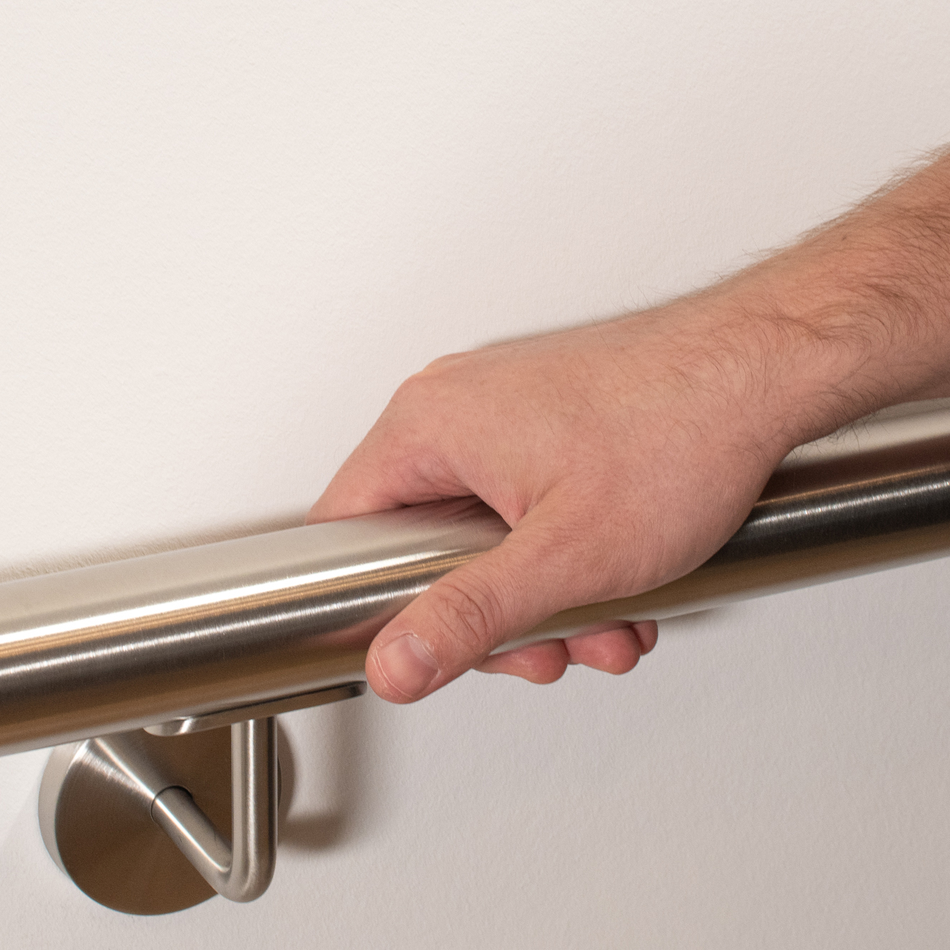 Edelstahlhandlauf rund an weißer Wand mit Edelstahl-Handlaufhalter, Hand umfasst den Handlauf, Nahaufnahme