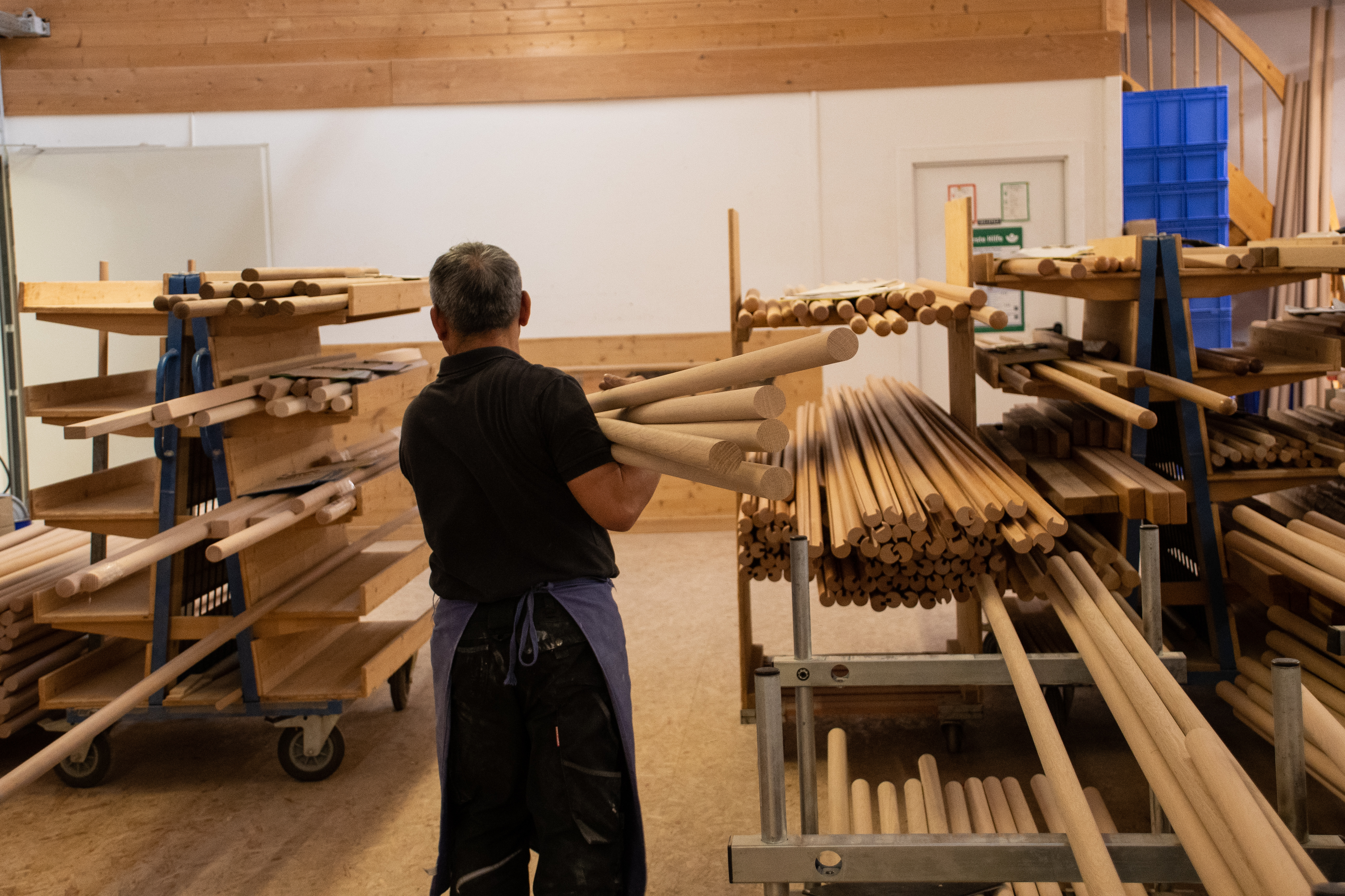 Rundstäbe aus Holz im Werkstattregal, Mitarbeiter sortiert Holzstäbe in der Drechslerei, viele Durchmesser