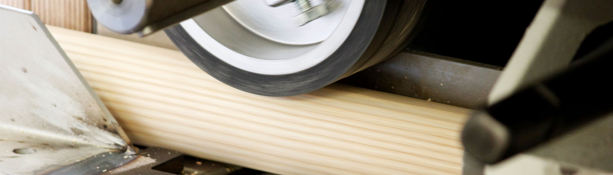Handlaufproduktion: Holz-Rundstab wird in der Schleifmaschine geschliffen, Nahaufnahme der Schleifwalze, Bannerformat
