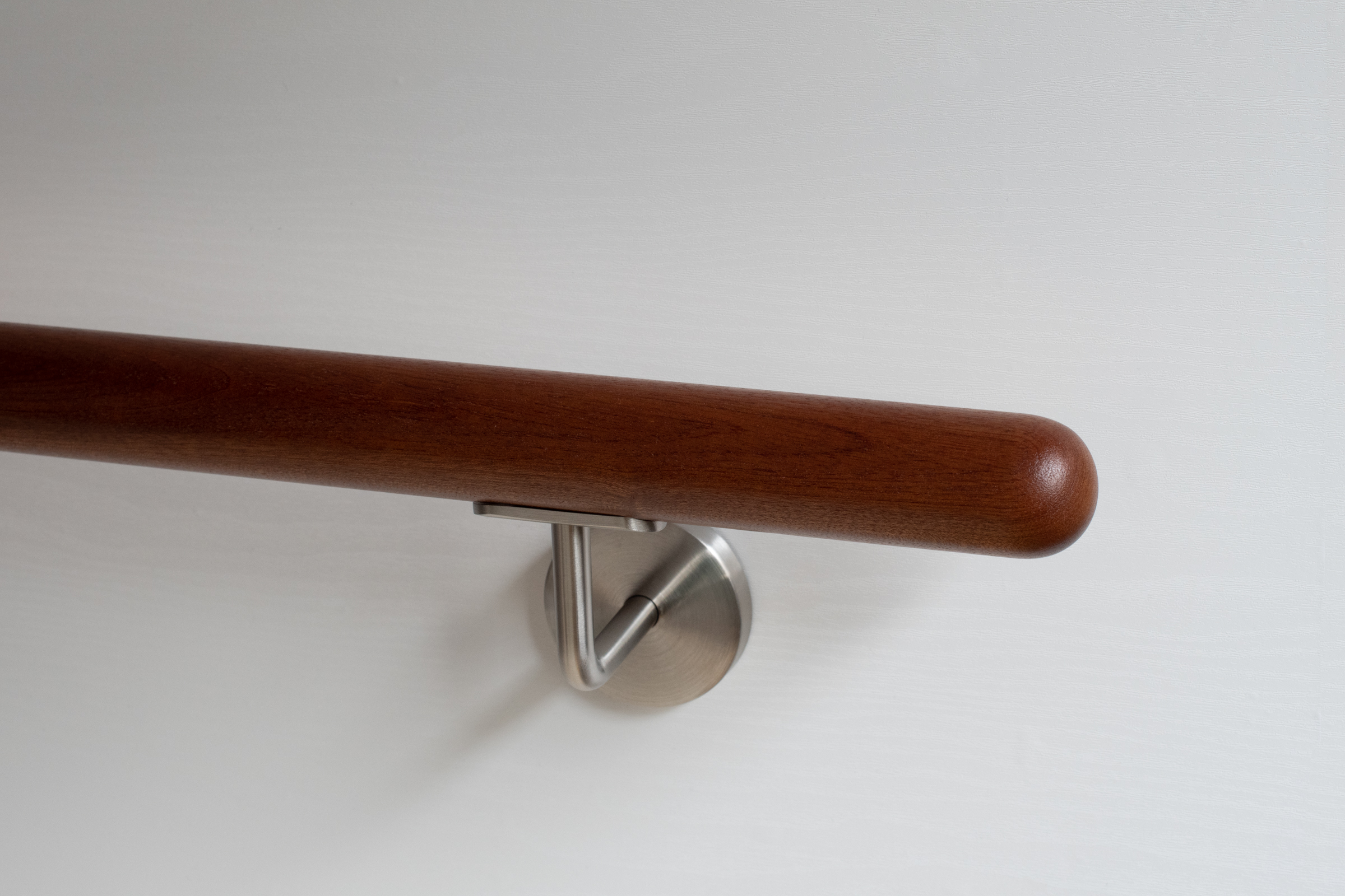 Handlauf Mahagoni rund mit Edelstahl-Wandhalter an weißer Wand, rotbraunes Holz, Nahaufnahme des abgerundeten Endes