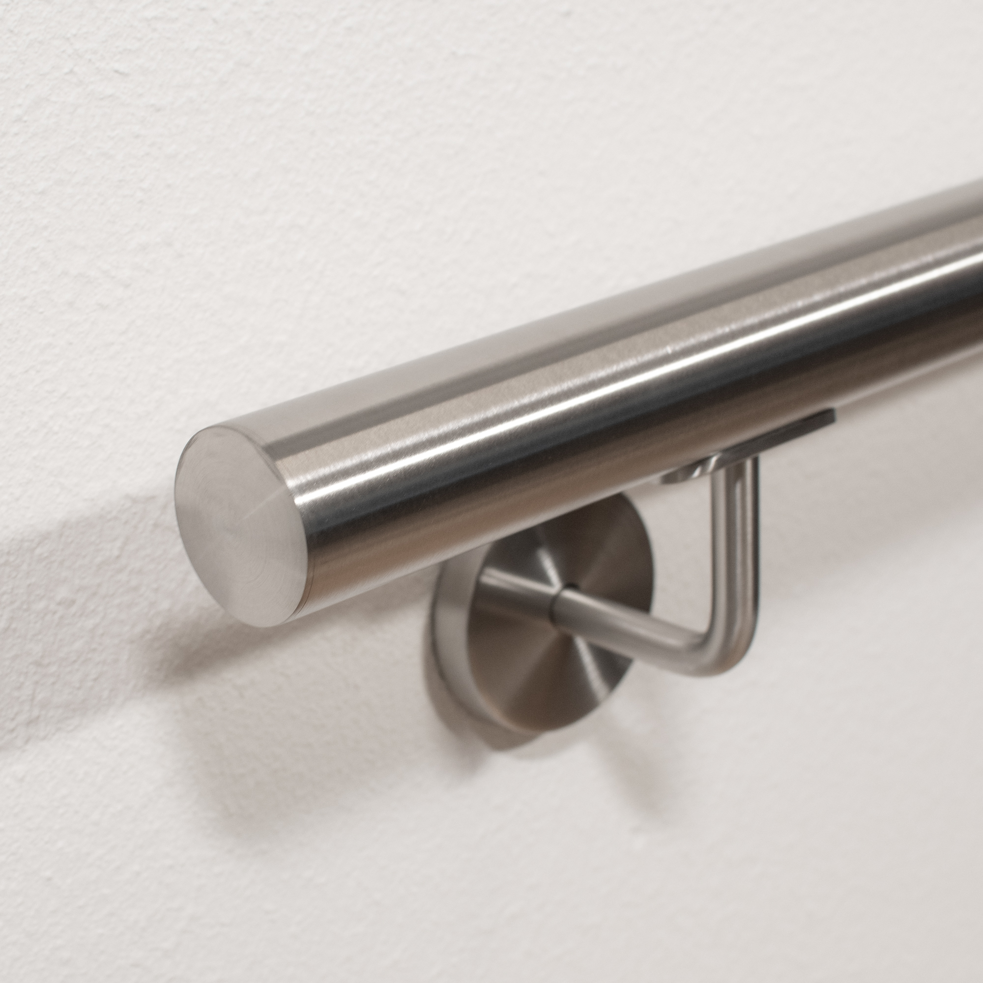 Handlauf Edelstahl rund mit Edelstahl-Wandhalter und flacher Endkappe an weißer Wand, Nahaufnahme von schräg unten