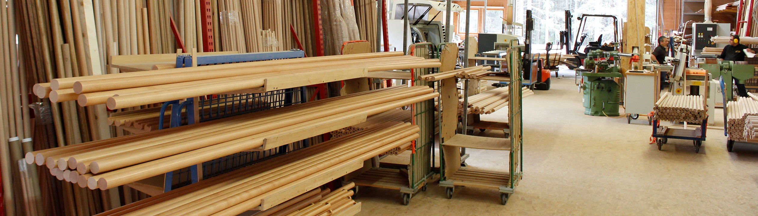 Handlaufproduktion: Lager mit hellen Holzhandläufen und Rundstäben auf Rollwagen in der Werkstatt, Bannerformat