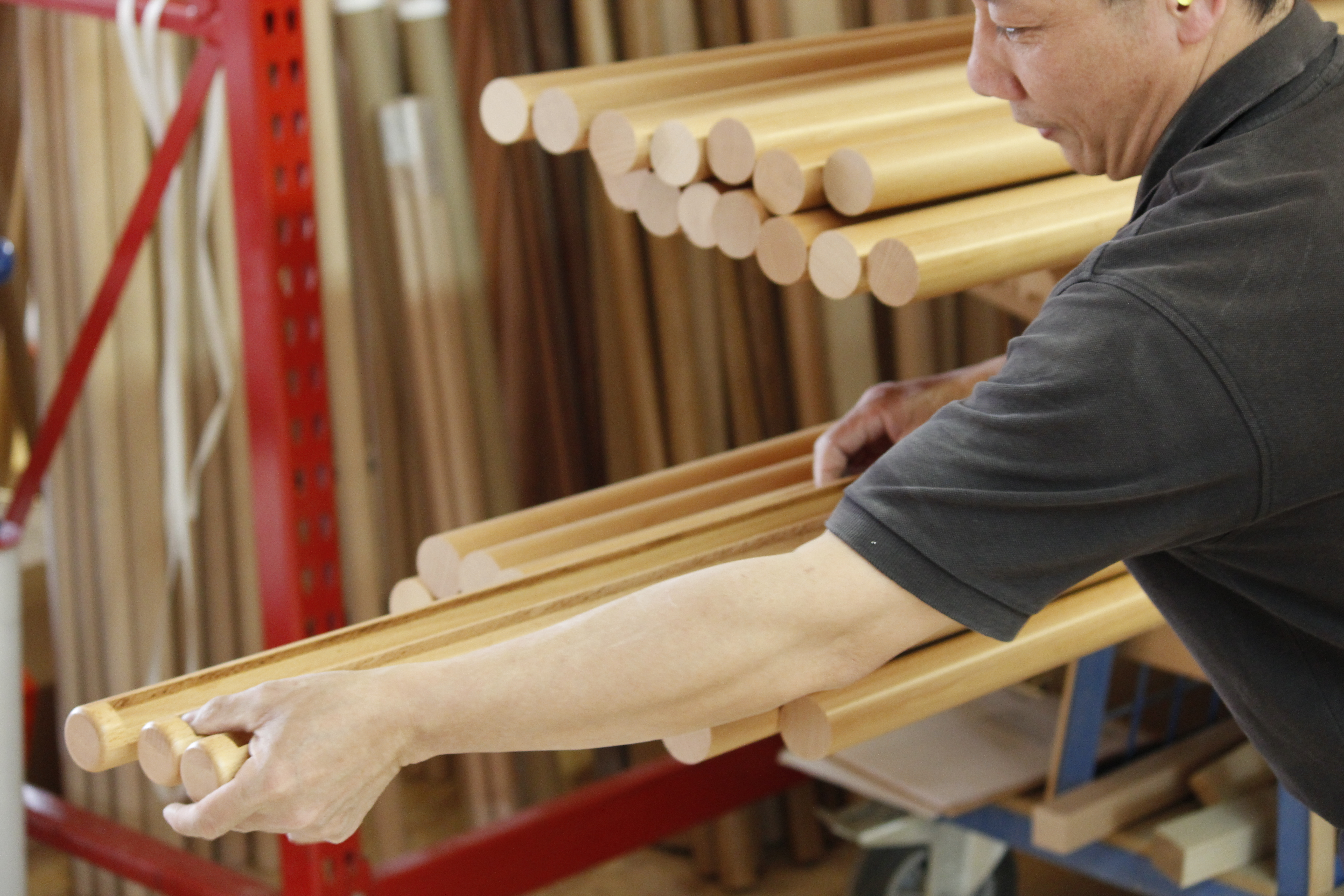 Qualitätskontrolle runder Holzhandläufe: Mitarbeiter prüft die Stäbe von Hand am Lagerregal in der Werkstatt