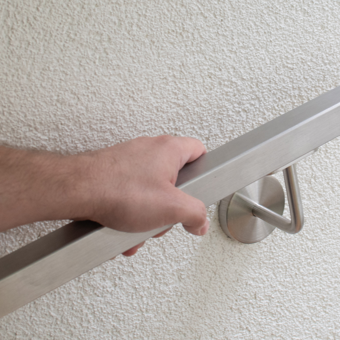 Handlauf Edelstahl quadratisch an verputzter Wand, Hand umfasst den Handlauf, Wandhalter Edelstahl mit Rosette