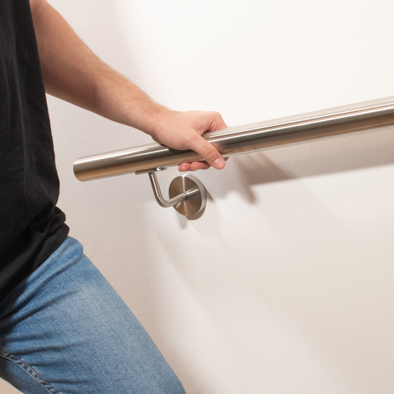 Edelstahlhandlauf rund an weißer Wand mit Edelstahl-Handlaufhalter, Person in Jeans hält sich am Handlauf fest