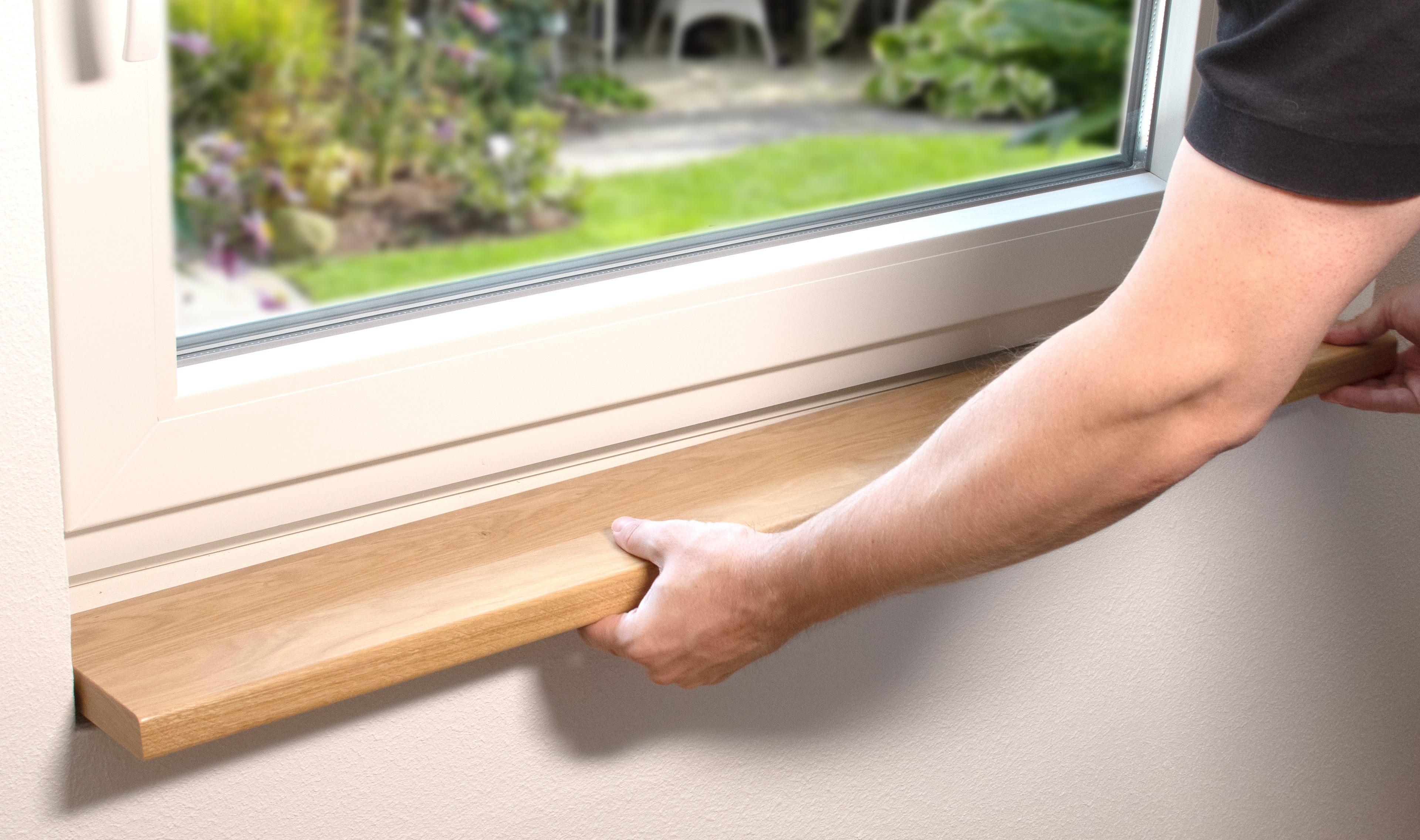 Fensterbank Massivholz beim Einbau: Hand setzt helle Holzfensterbank unter weißes Fenster, Blick in den Garten