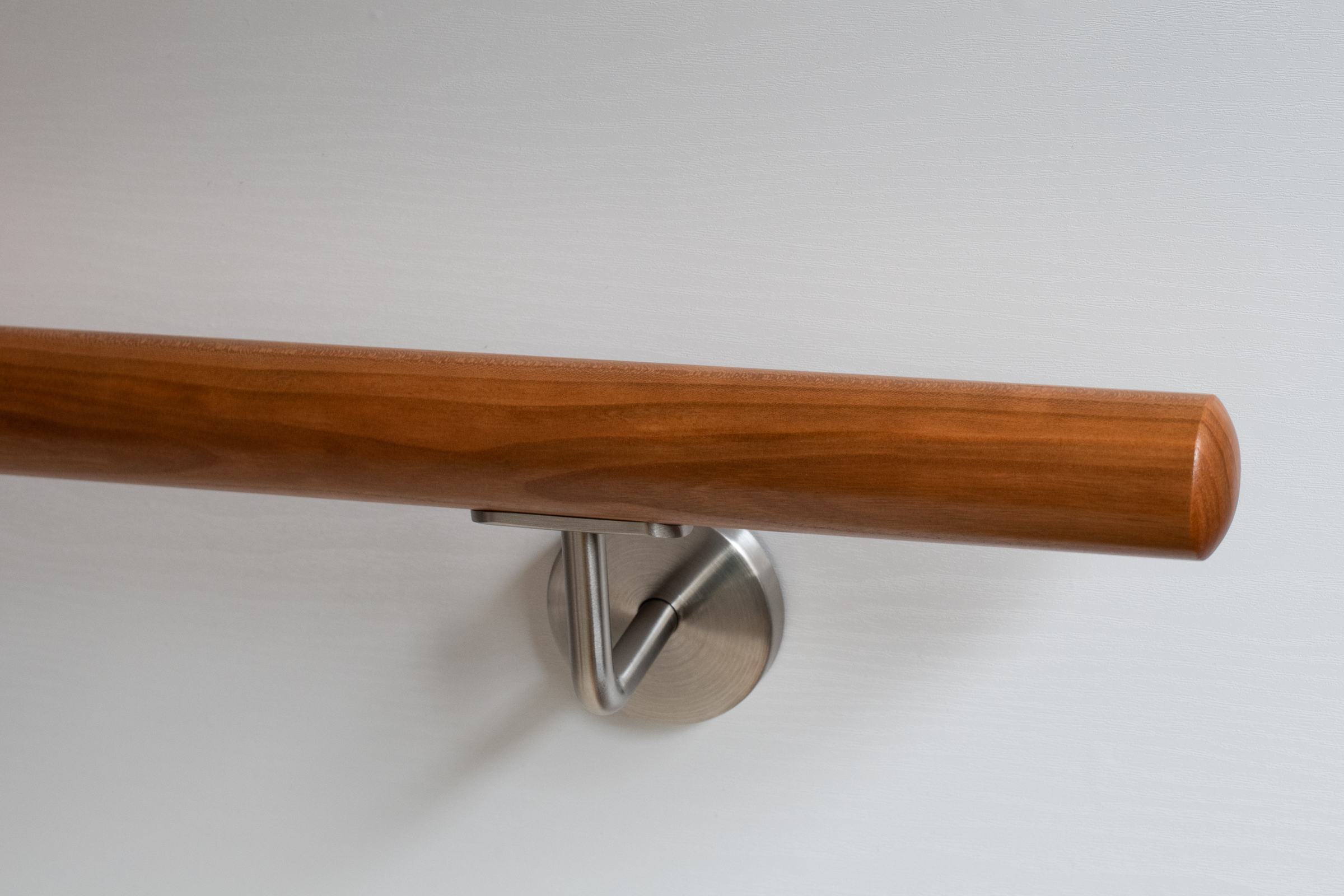 Handlauf Kirsche rund mit Edelstahl-Wandhalter an weißer Wand, warm rotbraunes Holz, Nahaufnahme des Endes