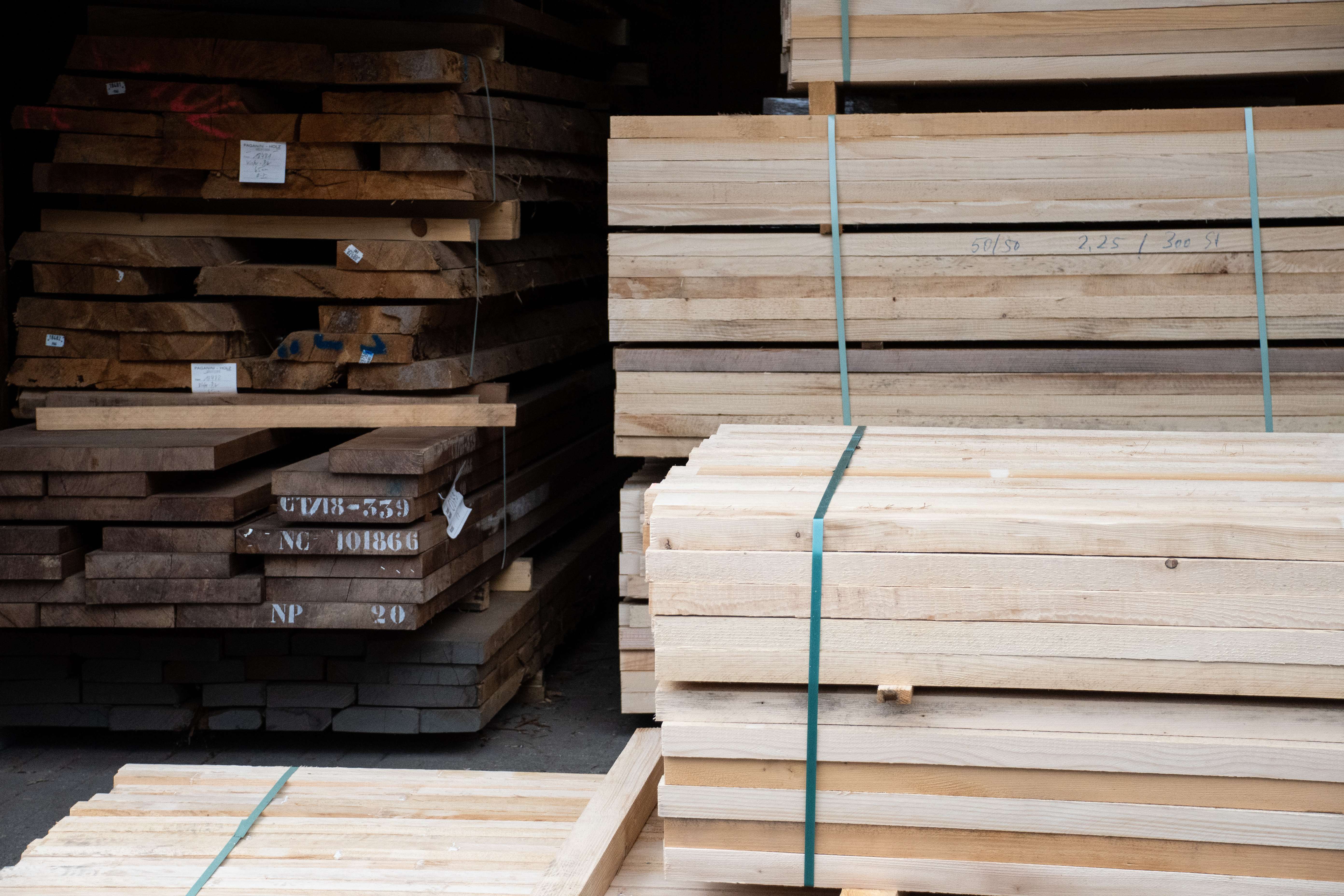 Holzlager mit gestapelten Massivholzbohlen und gebündelten hellen Brettern, Rohmaterial für Holzhandläufe